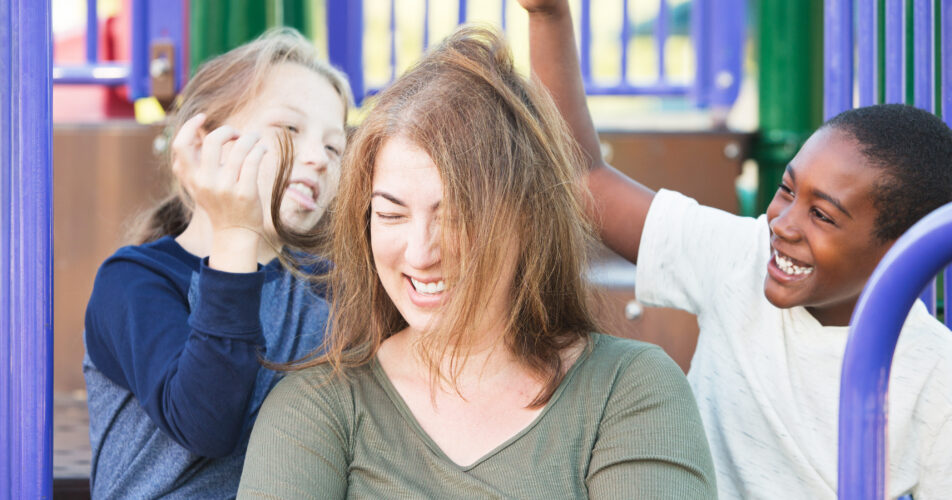 Silly,Children,Playing,With,Hair,Of,Laughing,Woman