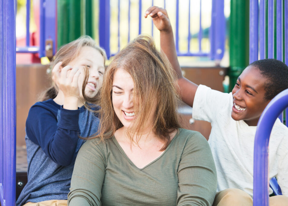 Silly,Children,Playing,With,Hair,Of,Laughing,Woman